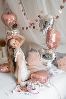Beautiful young girl at home on the bed in the morning enjoy valentines day celebration with heart shaped balloons. High quality photo