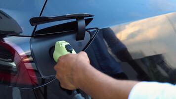 de cerca de negro del hombre mano, insertando un cargador dentro su lujo eléctrico coche y usos un móvil solicitud a controlar el batería video