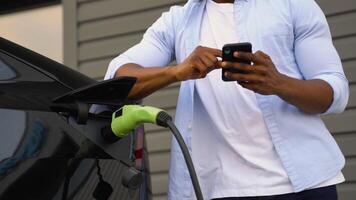 africano americano homem usa uma Móvel inscrição para ao controle a bateria do a elétrico carro video