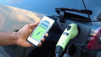 schwarz Mann Verwendet ein Handy, Mobiltelefon Anwendung zu Steuerung das Batterie von ein elektrisch Auto video