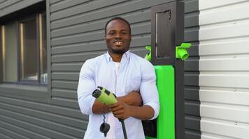 portret van glimlachen zwart Mens met een oplader Bij ev opladen station video