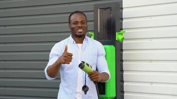 retrato do sorridente Preto homem com uma carregador às ev cobrando estação video