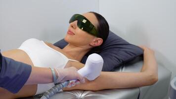 Calm young woman lying with closed eyes and putting on arm up while having laser hair removal procedure on it video