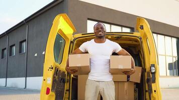 Portrait of a black courier holding a two parcels, a yellow car in the background video