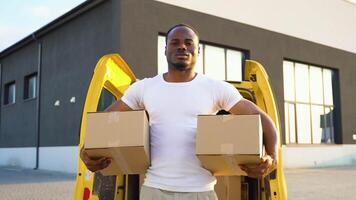Portrait of a black courier holding a two parcels, a yellow car in the background video