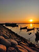puesta de sol en paiton playa con siluetas de pescar barcos anclado en el puerto foto