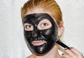 niña en un cosmético negro mascarilla. limpieza máscara de aspirina y activado carbón. negro cosmético cara mascarilla. foto