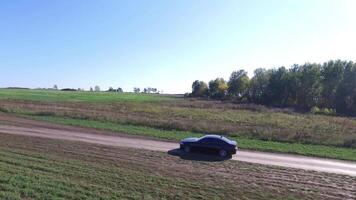 The car is going on the road through the field aerial view. Footage. Car goes on the sunlit road through fields and forests. View from the side of the road video