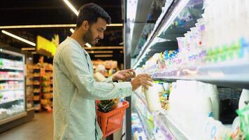 Side view of handsome indian man buying milk. A man shopping dairy product in grocery store video