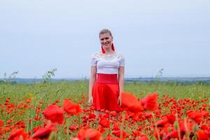 rubia joven mujer en rojo falda y blanco camisa, rojo pendientes es en el medio de un amapola campo. foto