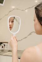 un sonriente mujer mira en el espejo en el de cosmetóloga oficina. vertical foto