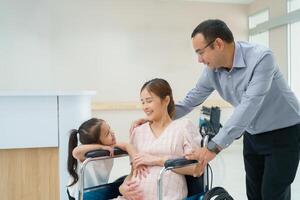 asiático marido tomando cuidado de embarazada mujer sentado en silla de ruedas y niños sonrisa a hospital foto