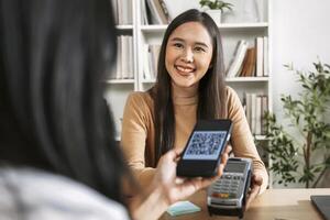 joven asiático mujer sonriente y pago con teléfono inteligente en restaurante foto