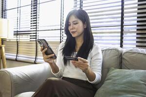 felizmente relajado joven mujer se sienta en un sofá utilizando un móvil teléfono foto