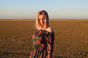 Woman in a plowed field in a red-black dress on a sunset background. photo