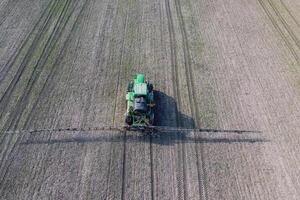 Tractor with hinged system of spraying pesticides. Fertilizing with a tractor, in the form of an aerosol, on the field of winter wheat. photo