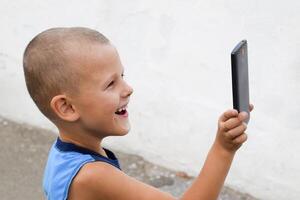 niño con un teléfono inteligente un pequeño chico dispara vídeo en un teléfono inteligente foto