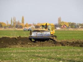 The yellow tractor with attached grederom makes ground leveling. photo