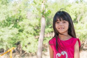 Beautiful latin kid smiling for a photo, in a park full of trees and green tones. photo