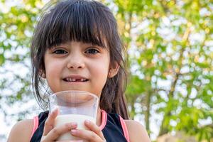 de cerca retrato de su. ella bebidas un vaso de frío Leche después jugando fuera de su casa. foto