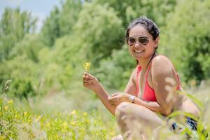 retrato de un argentino latín mujer participación un flor mientras sonriente. foto