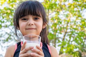 de cerca retrato de su. ella bebidas un vaso de frío Leche después jugando fuera de su casa. foto