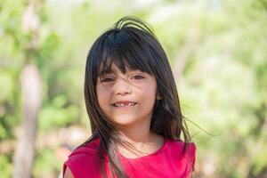 retrato de un sonriente latín niño mirando a el cámara con su pelo soplo en el viento en un parque. foto