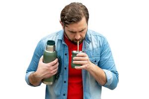 Young man drinking mate, carrying the thermos in his arm. photo