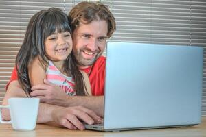 retrato de un padre y su hija riendo en frente de el computadora. foto