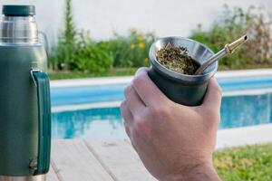 Young man drinking mate in the morning in front of the pool. photo