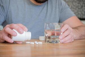 hombre sentado en el cocina con un vaso de agua para tomando su pastillas foto