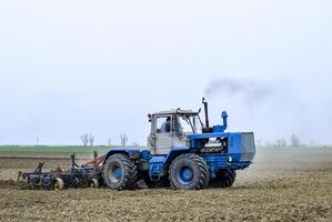 lozano y aflojar el suelo en el campo antes de siembra. el tractor arados un campo con un arado foto