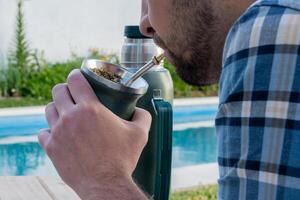 Young man drinking mate in the morning in front of the pool. photo