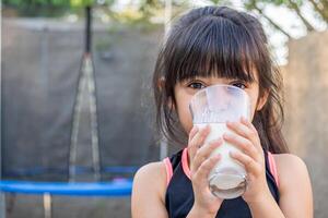 Close-up portrait of her. She drinks a glass of cold milk after playing outside her house. photo