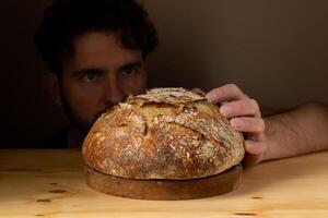 atractivo joven caucásico cocinero posando con blanco de masa fermentada un pan. el de masa fermentada un pan es el central protagonista de el escena, en pie fuera con hermosa dorado tonos en contra el oscuro antecedentes. foto