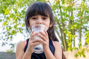 de cerca retrato de su. ella bebidas un vaso de frío Leche después jugando fuera de su casa. foto