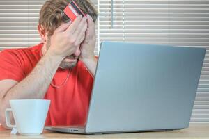 Portrait of a man watching his computer frustrated with credit card in hand. photo