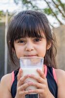 de cerca retrato de su. ella bebidas un vaso de frío Leche después jugando fuera de su casa. foto