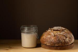 Jar of sourdough on a table, accompanied by fresh, crusty sourdough bread. photo