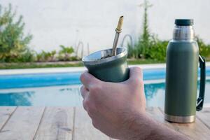 Young man drinking mate in the morning in front of the pool. photo