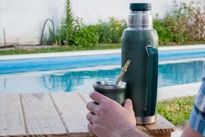 Young man drinking mate in the morning in front of the pool. photo