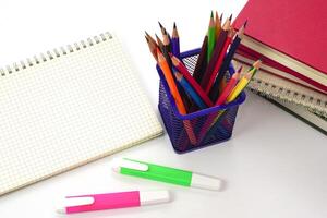 Crayon or colored pencils in box with side stack of books and school supplies on with background. Learning, study and office equipment concept. photo