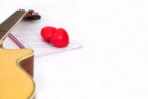 Focus the red heart and blur musical notes and acoustic guitar neck on white background. Love, music and learning concept. photo