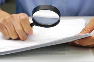Focus magnifying glass, Hand of businessperson looking at documents through magnifying glass. Concept of business and data validation. photo