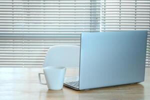 Laptop and cup on the table in the morning with a background of American blinds. photo