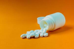 Pills spilling out of the container on a bright orange background. photo