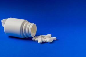 Prescription bottle with white pills on a blue background. photo