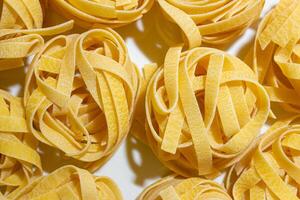 Uncooked Egg-Based Fettuccine Pasta. A Culinary Canvas of Ribbon-Shaped Macaroni, Creating a Lively and Textured Background for Gourmet Cooking. Dry Pasta. Raw Macaroni - Top View, Flat Lay photo