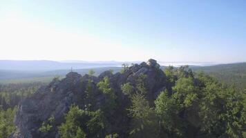 Fir, birch and pine tree forest over rocks seen from above. Beautiful summer landscape with rock and forest around, aerial view video