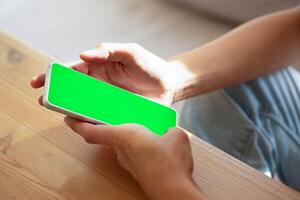 White smartphone with green screen in female hands close up. Online working, shopping. Chroma key. photo